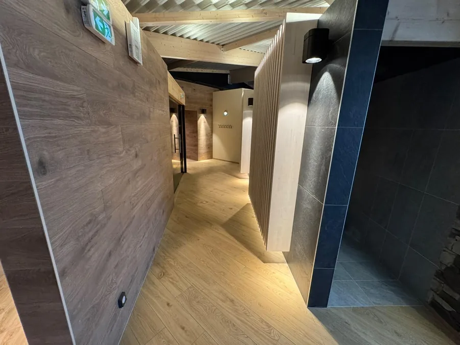 Couloir de spa avec habillages bois, carrelage et éclairage architectural